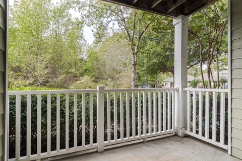 A white wooden fence on a porch with a view of trees.