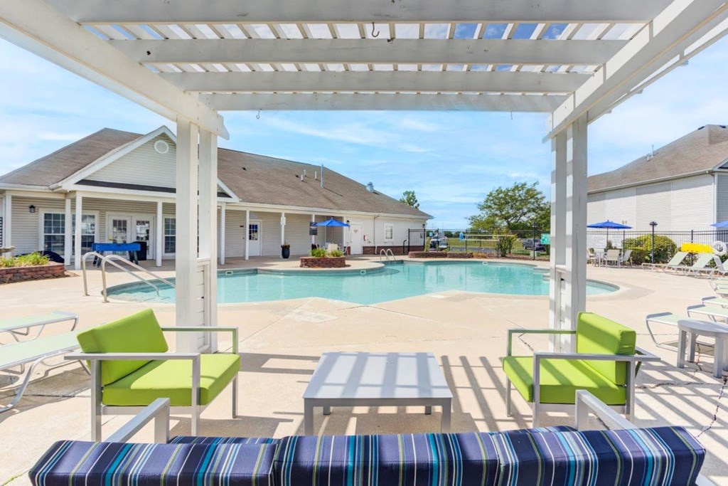 A pool area with a white pergola and a striped bench.