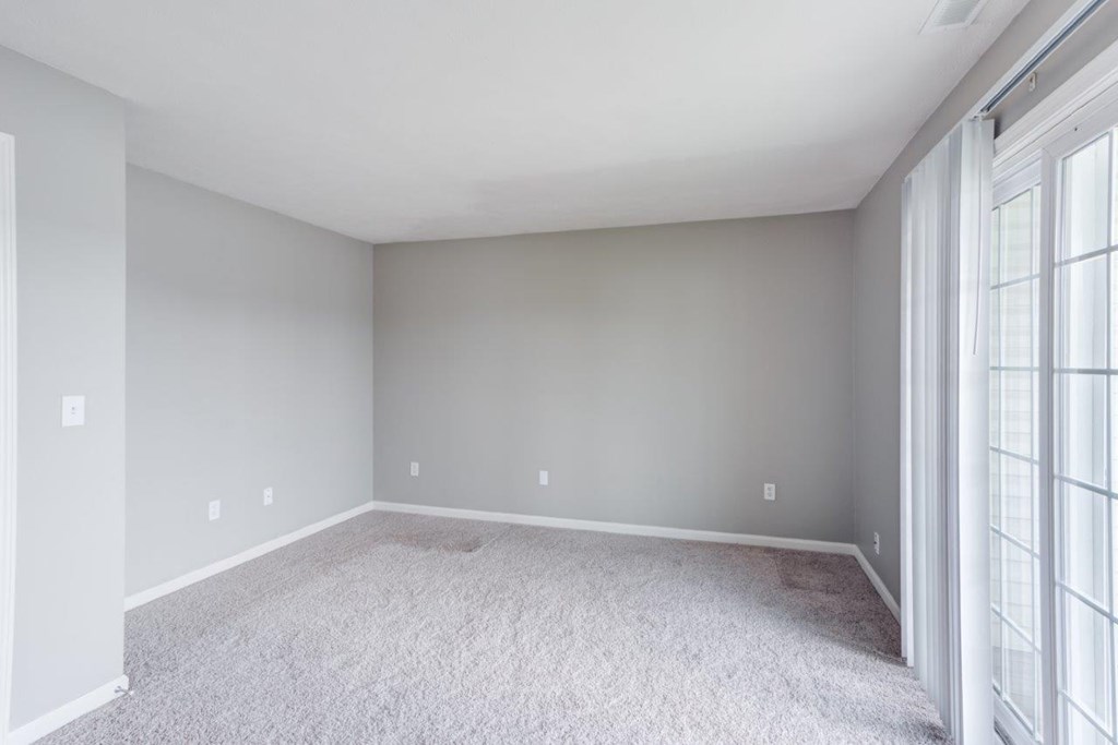 A room with a carpeted floor and a window with blinds.