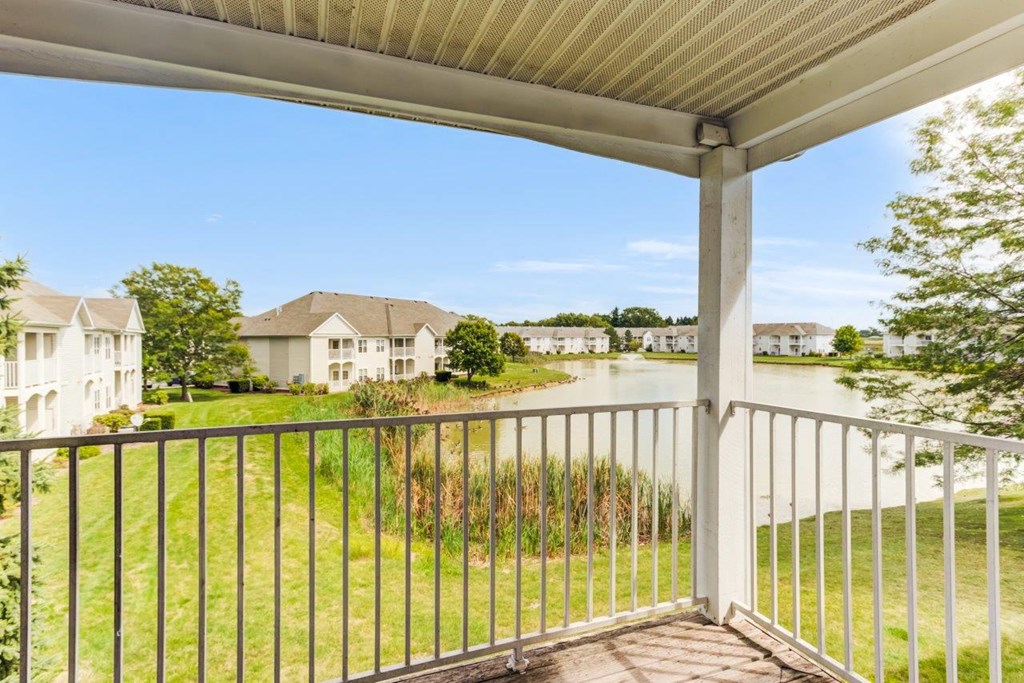 A balcony with a metal railing overlooks a grassy area and houses.