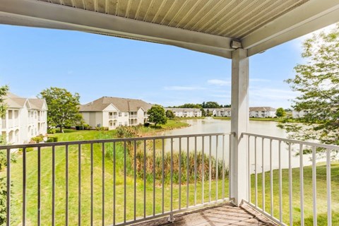 A balcony with a metal railing overlooks a grassy area and houses.