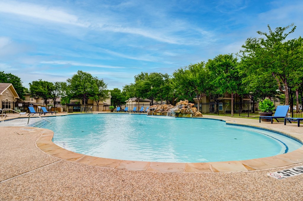 our resort style swimming pool is surrounded by chairs and trees