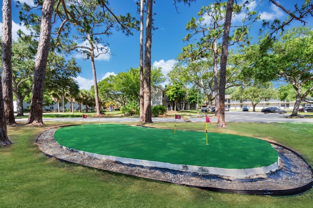 a putting green in a park with trees and a parking lot