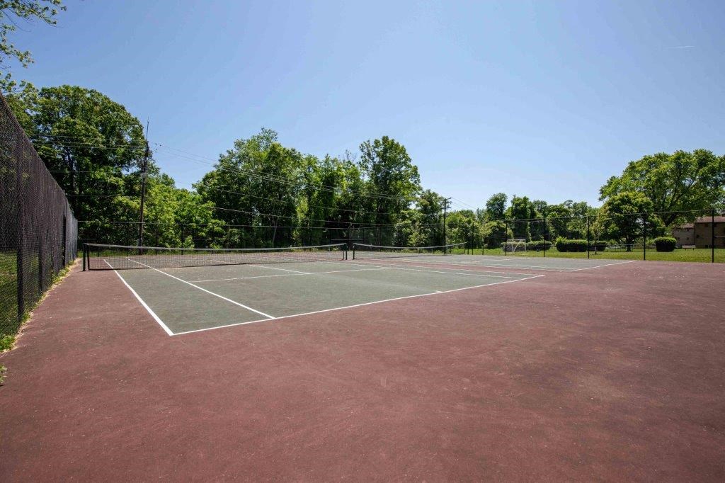a tennis court with a fence and trees in the background on a clear day