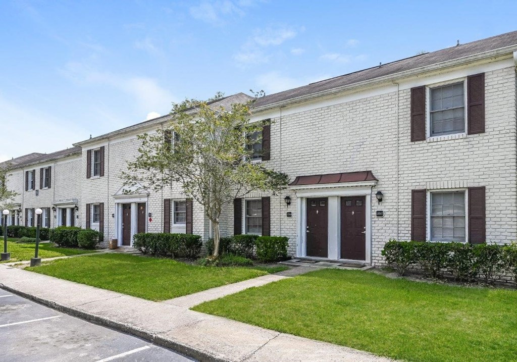 the front of a white brick house with a lawn and trees