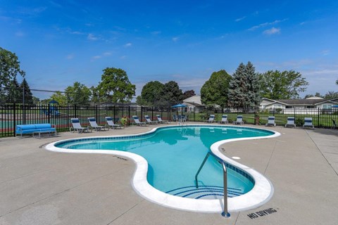A large outdoor swimming pool surrounded by a fence and lounge chairs.