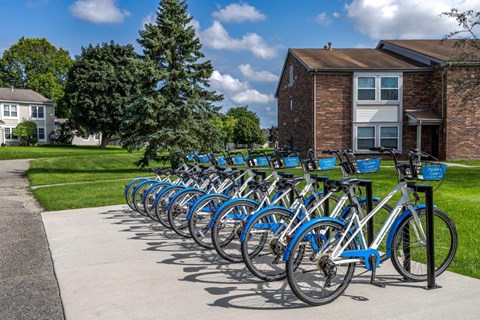 A row of blue bicycles are parked in front of a brick building.