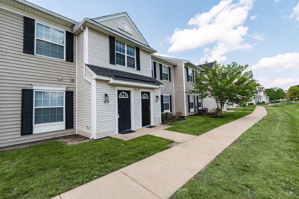 a sidewalk in front of a row of homes with grass and trees