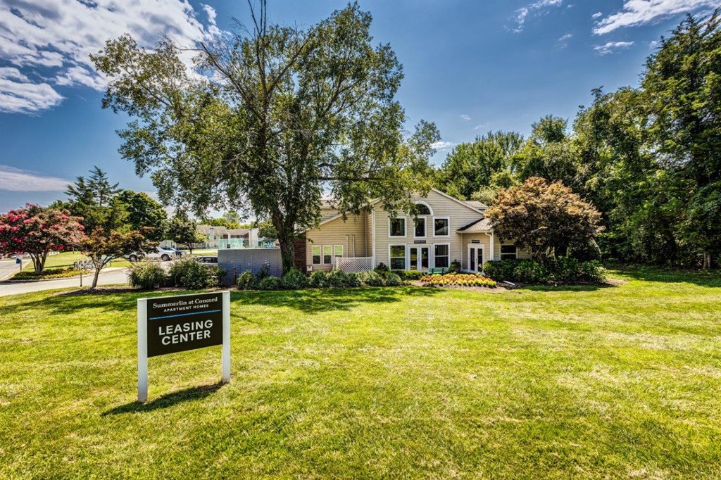 A leasing center sign is in the foreground of a well-kept lawn with a building in the background.