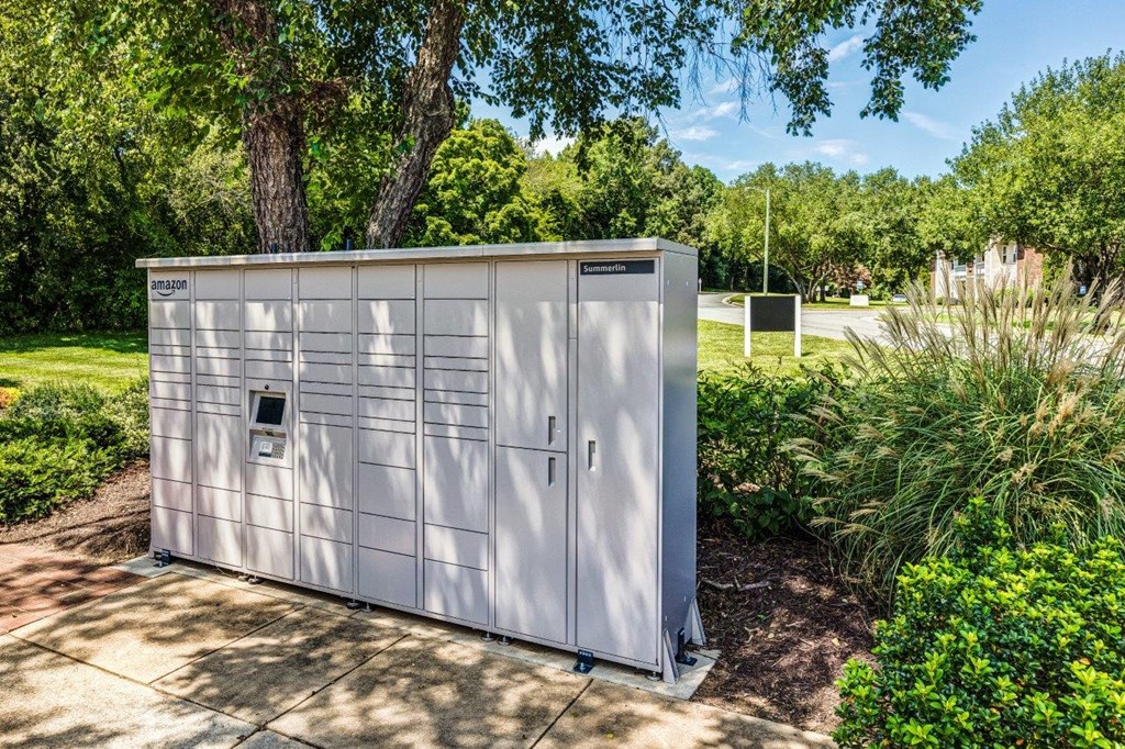 A large, white, metal storage unit with a door and a window is situated on a concrete slab in a garden.