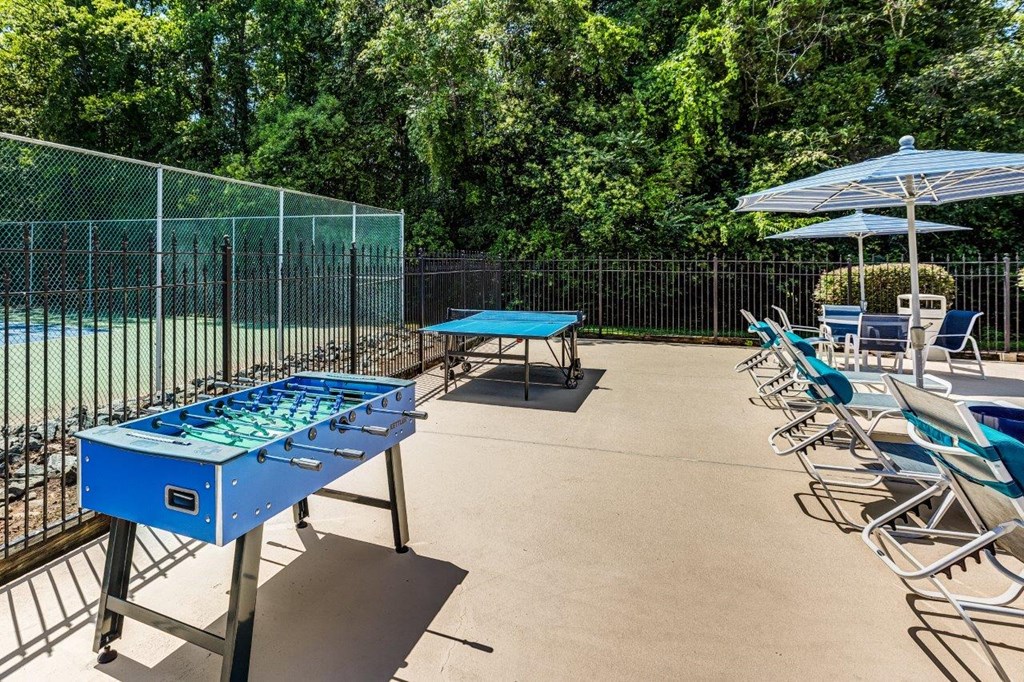 A blue table tennis table is surrounded by chairs and umbrellas.