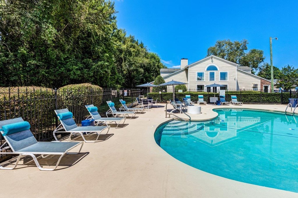 A pool with chairs and a house in the background.
