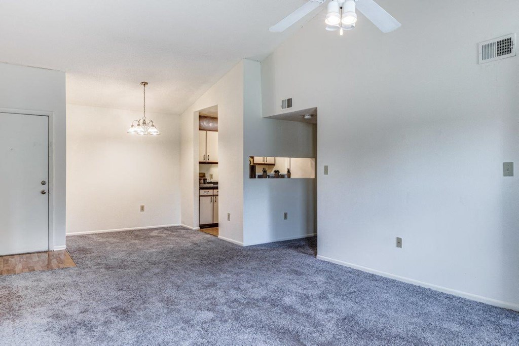 A spacious living room with a ceiling fan and a kitchen area in the background.