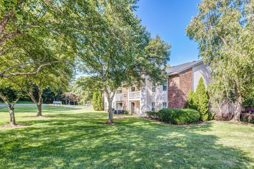 A house with a green lawn and trees in front.