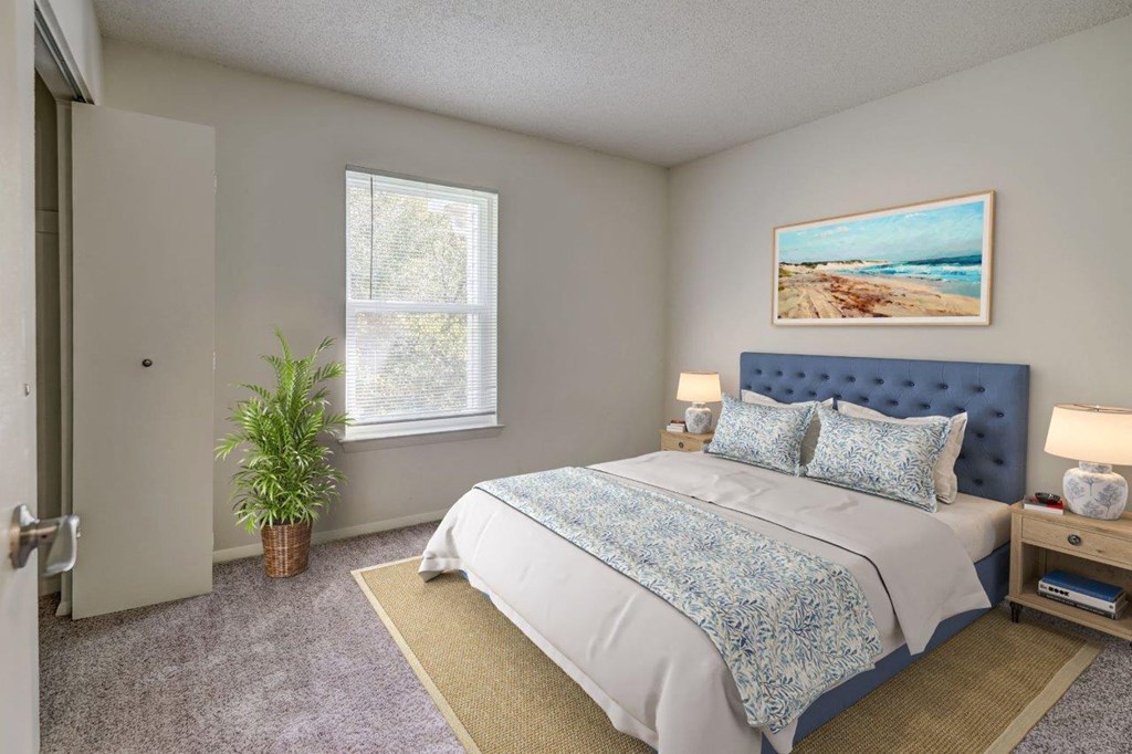 A bedroom with a bed, nightstand, and a plant.