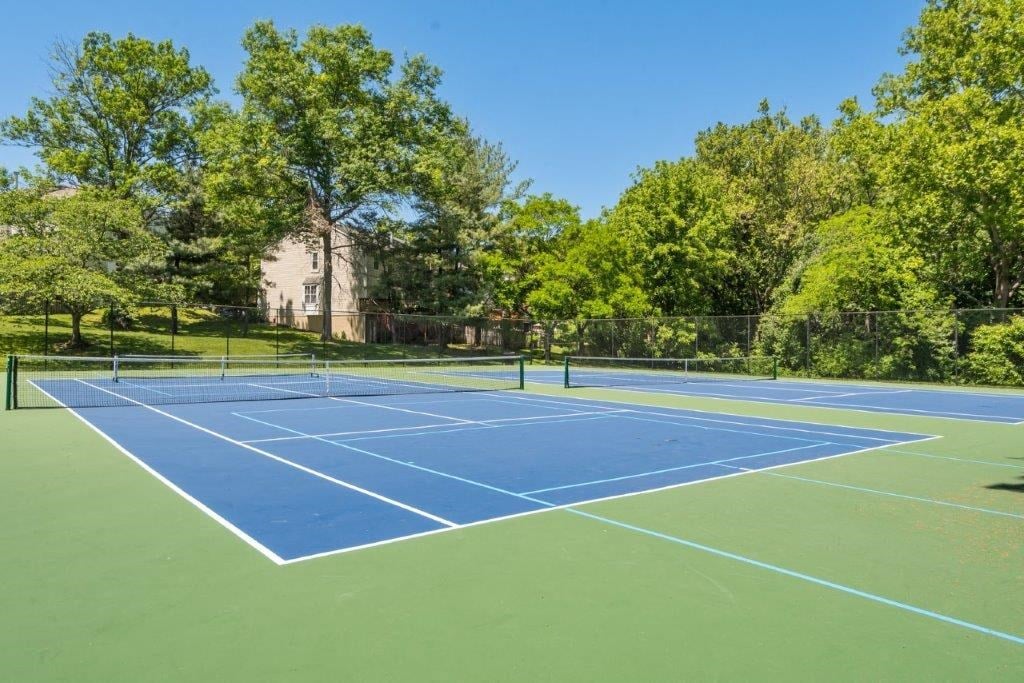 two tennis courts with trees and a building in the background