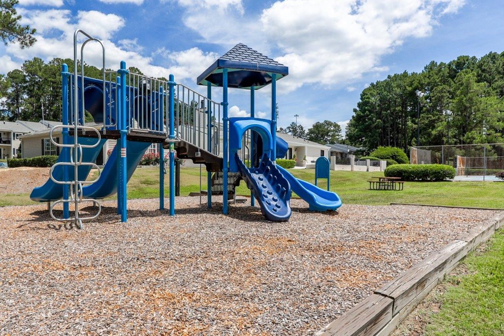 a playground with a blue playset and slides in a park