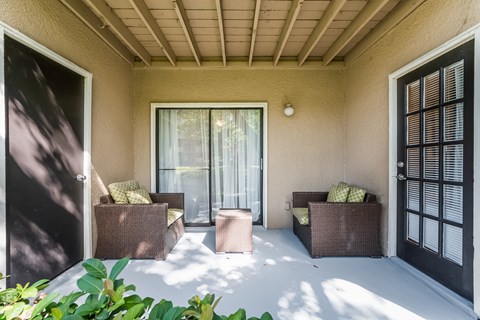 a covered porch with chairs and a glass door