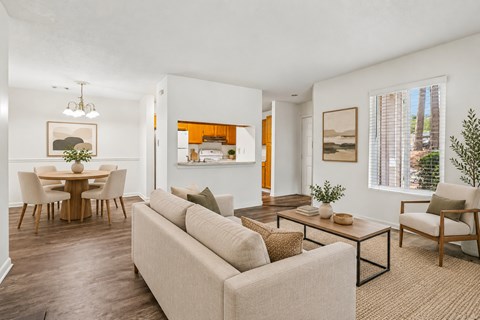 A living room with a beige couch, a wooden dining table with chairs, and a painting on the wall.