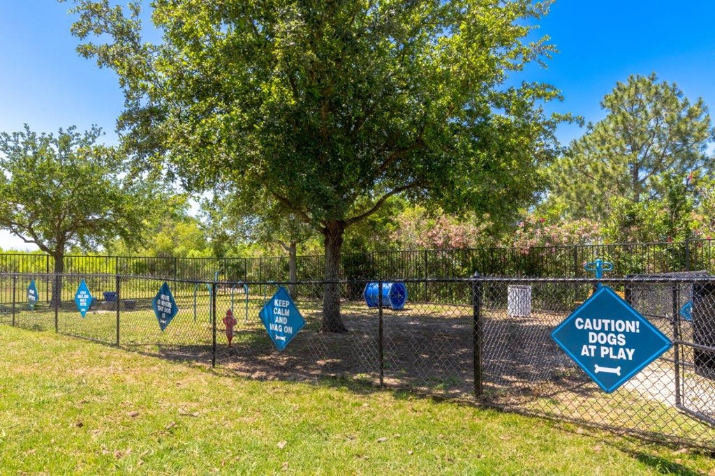 a dog park with blue signs on a fence and a tree