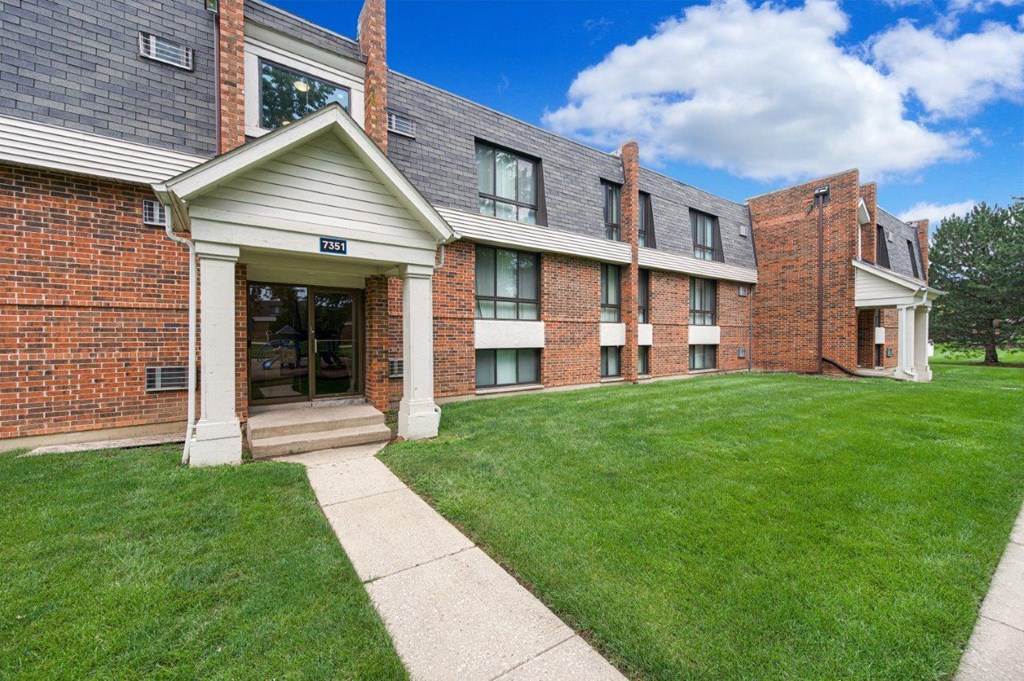 A brick building with a white entrance and a green lawn in front.