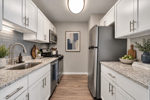 A kitchen with white cabinets and a grey refrigerator.