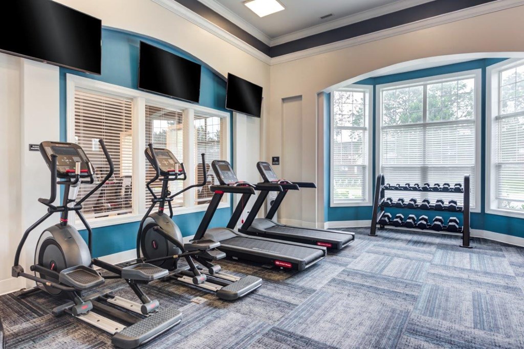 a gym with treadmills and other exercise equipment in a room with windows