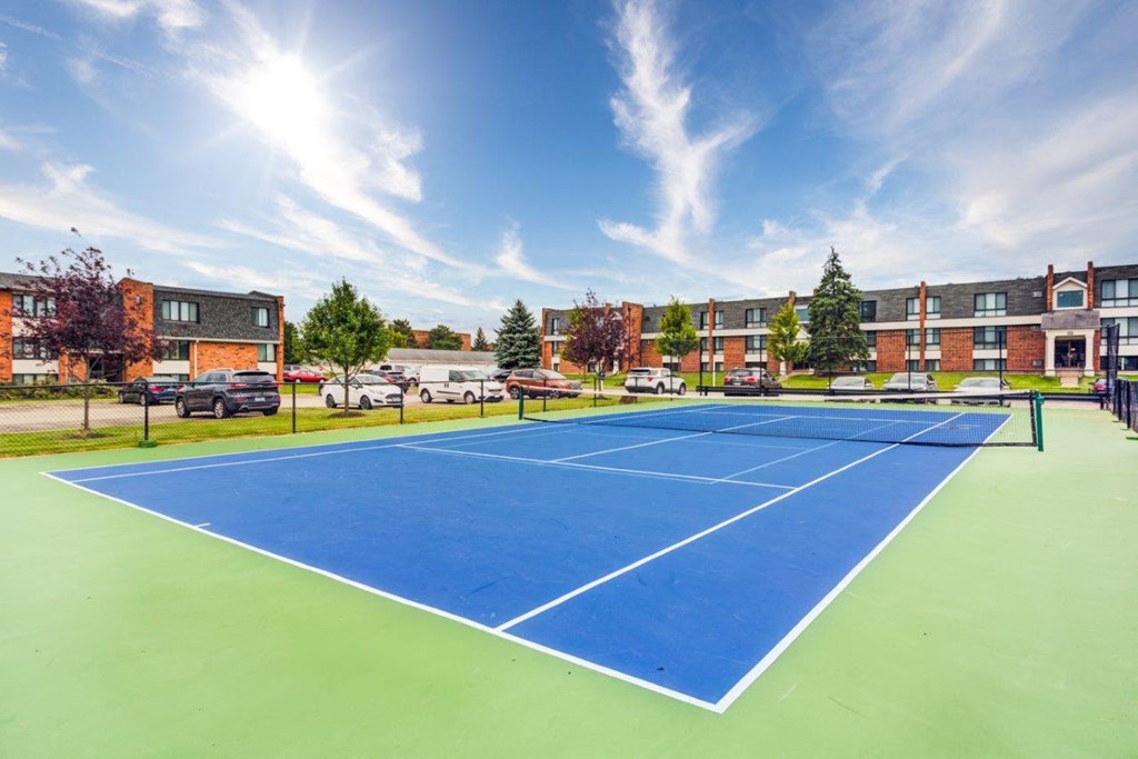 a blue and green tennis court with apartments in the background