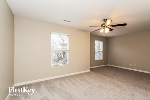 A spacious room with a ceiling fan and two windows.