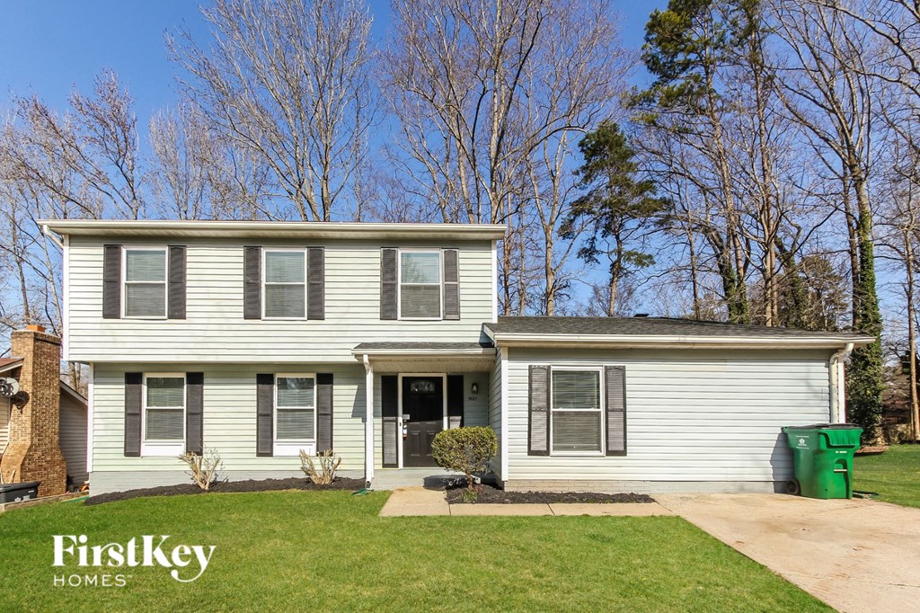 A two-story house with a grey siding and a green trash can in front.