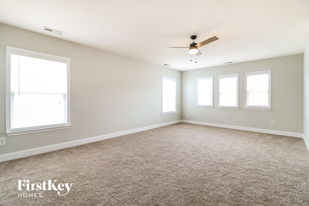 an empty living room with a ceiling fan and three windows