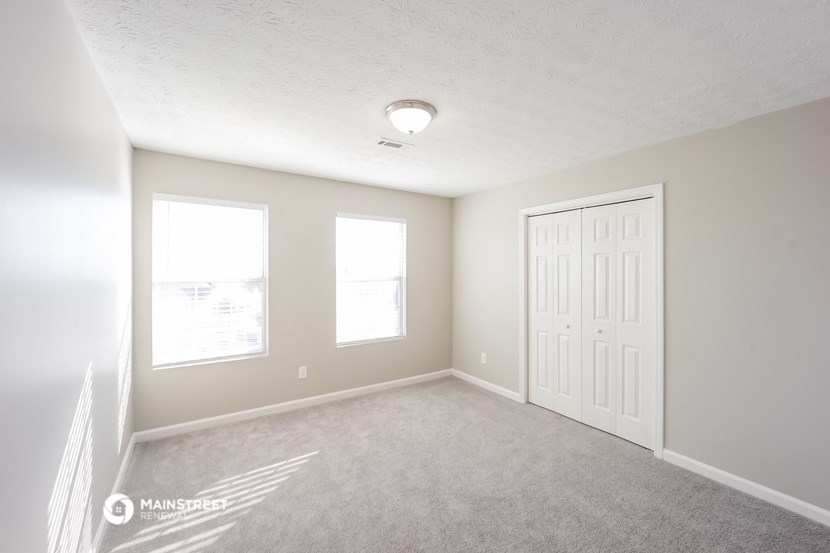 an empty room with a white door and two windows