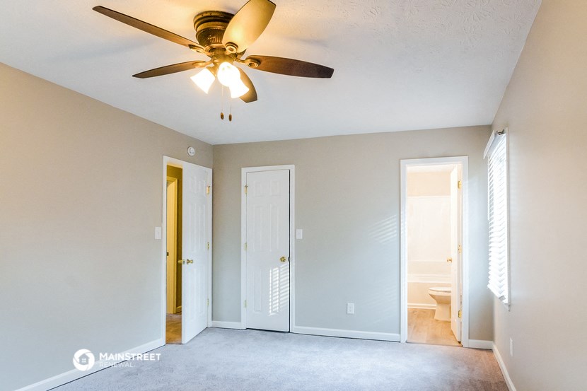 an empty living room with a ceiling fan and a door to a bathroom
