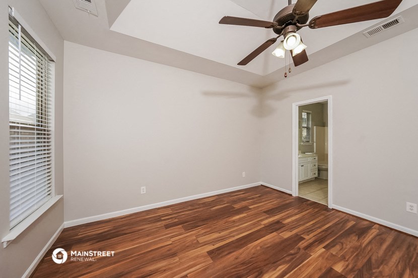 the spacious living room with hardwood flooring and a ceiling fan