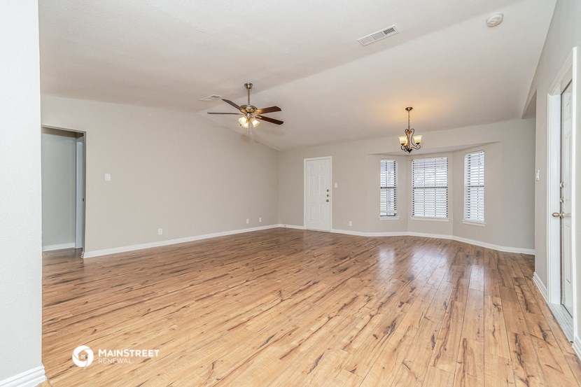 the spacious living room with hardwood flooring and a ceiling fan