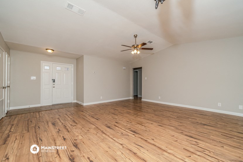 the spacious living room with hardwood floors and a ceiling fan