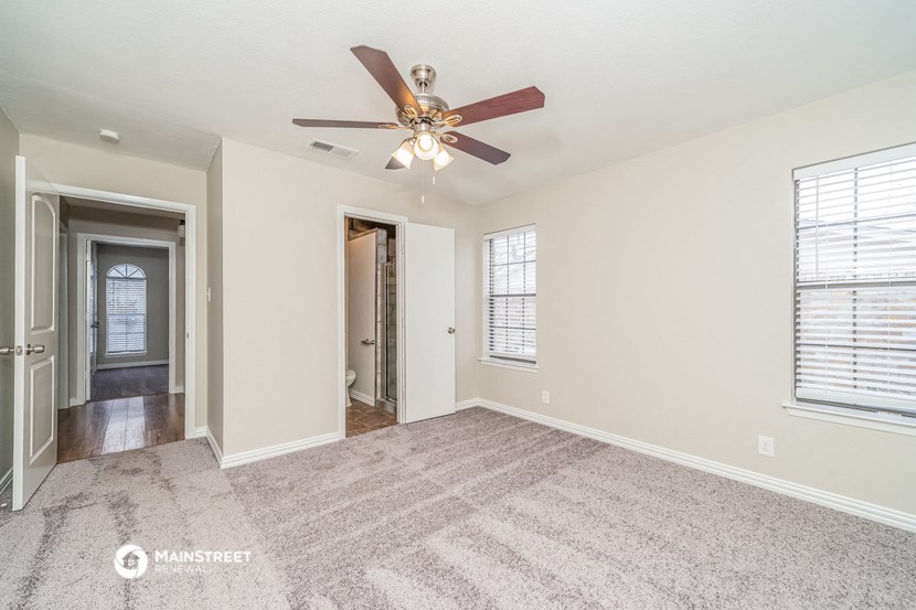 an empty living room with a ceiling fan and a hallway