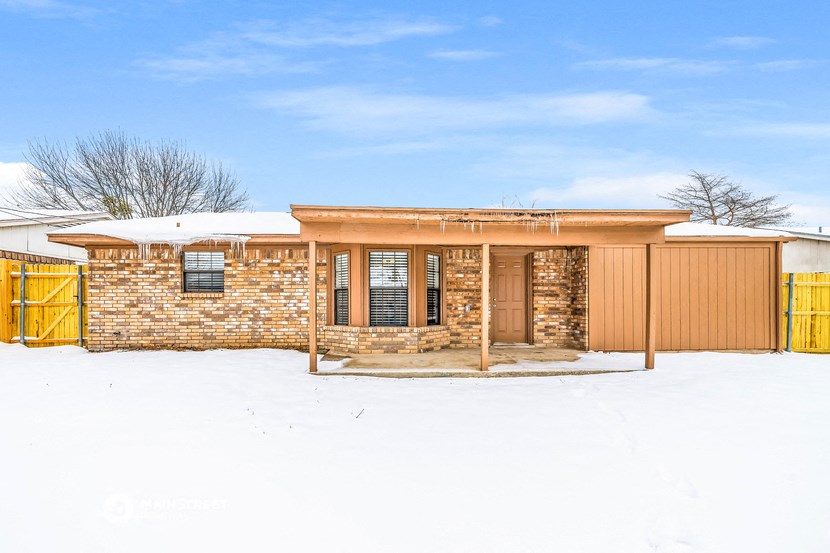 a small brick house with a wooden fence in the snow