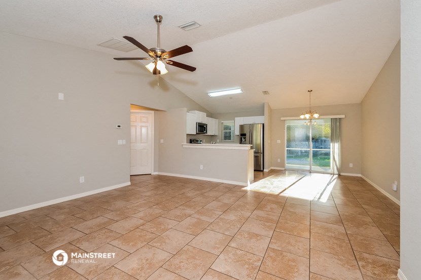 an empty living room with a ceiling fan and a kitchen