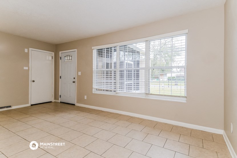 the living room of a home with a large window and tiled floors