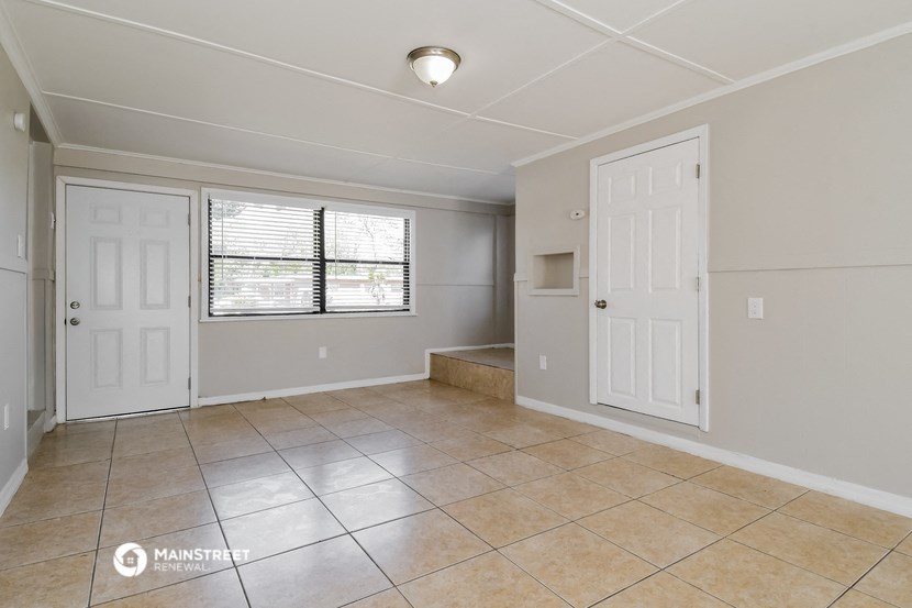 the spacious living room and dining room with a large tiled floor and two doors