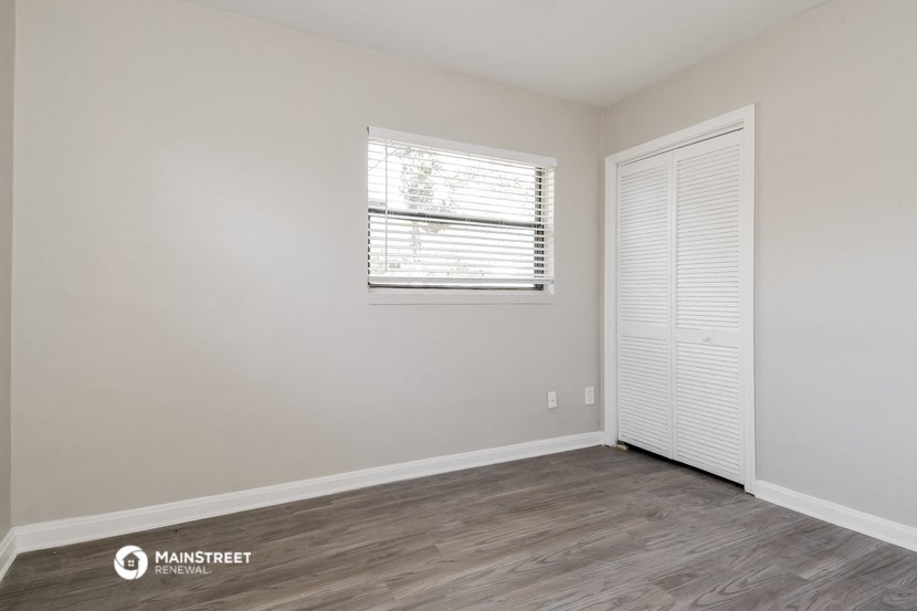 a bedroom with white walls and wood flooring and a window