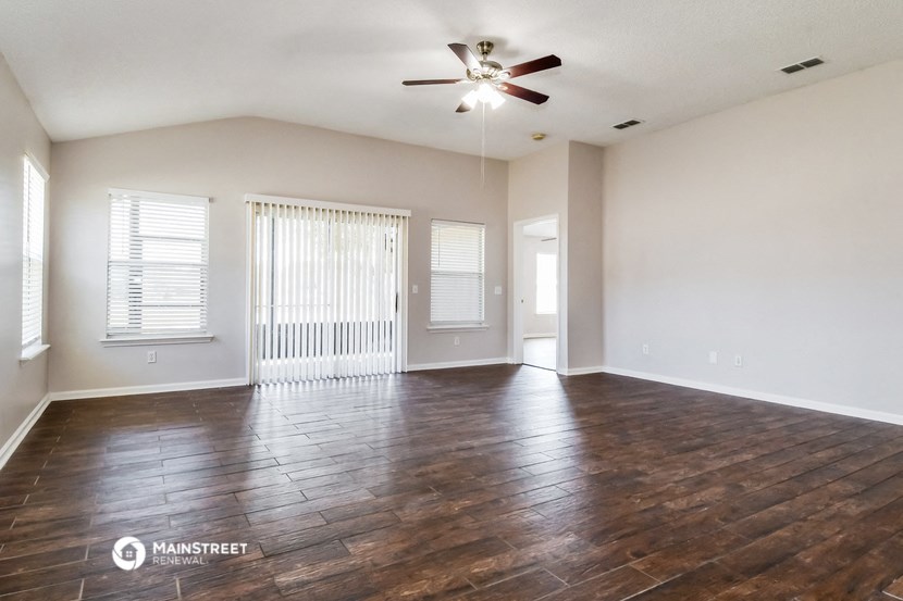 the spacious living room with wood flooring and a ceiling fan