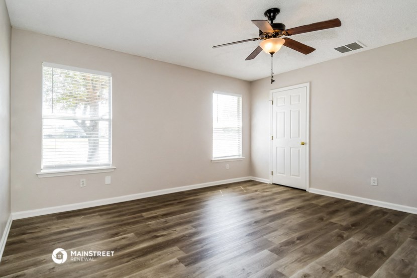 the spacious living room with wood flooring and a ceiling fan