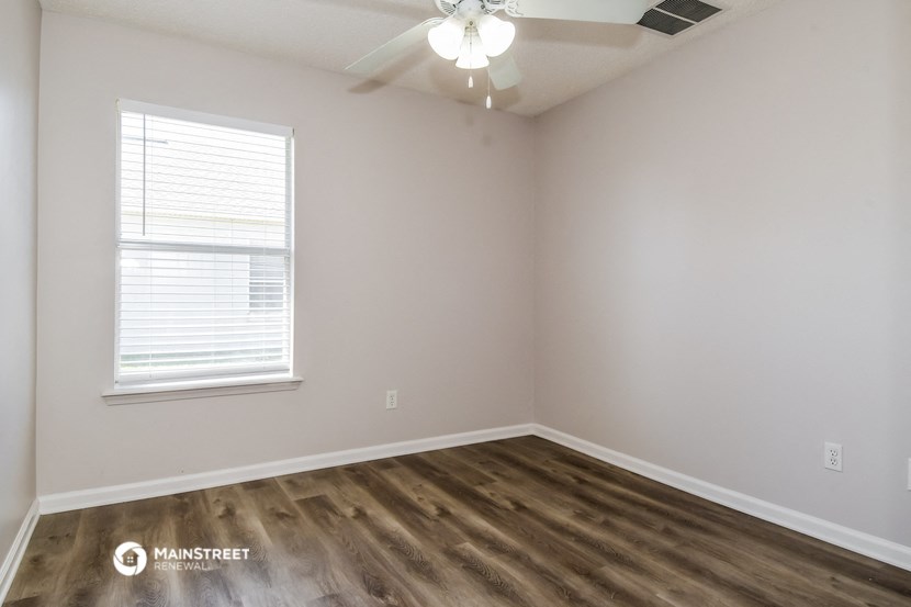 the bedroom of an apartment with wood flooring and a ceiling fan