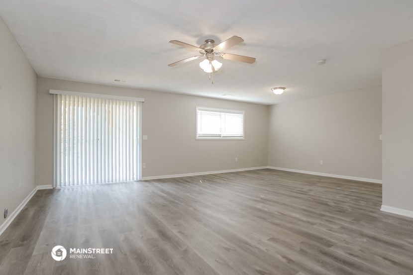 the spacious living room with wood flooring and a ceiling fan