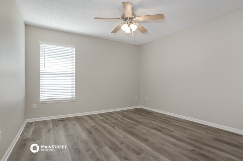 the spacious living room with hardwood flooring and a ceiling fan