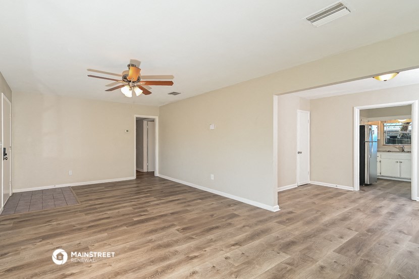 the spacious living room with wood flooring and a ceiling fan