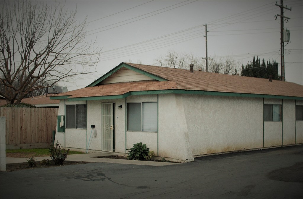 a small white building with a door and a street in front of it