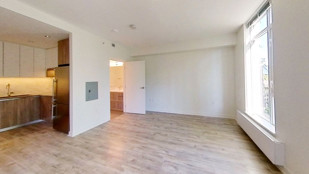 an empty living room with a large window and a kitchen